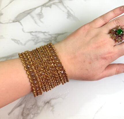 Traditional gold-plated bangles set with intricate detailing, elegantly worn on a woman’s wrist for a festive or cultural occasion