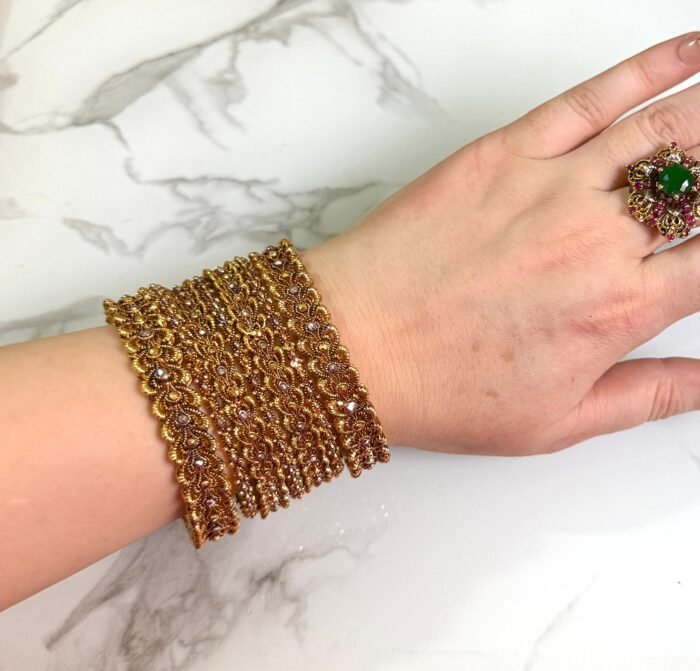 Traditional gold-plated bangles set with intricate detailing, elegantly worn on a woman’s wrist for a festive or cultural occasion