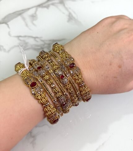 Hand adorned with gold-plated bangles featuring red crystal accents in a bow-style design
