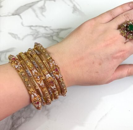 Luxury gold-plated bangle set with maroon stone detailing and elegant traditional patterns, displayed on a woman’s