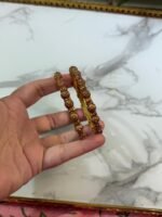 A pair of intricately designed antique copper-toned bangles with dome-shaped bead detailing, held in hand against a white marble background with a gold-edged tray.