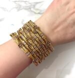 A hand adorned with eight gold bangles showcasing intricate chevron engravings and shimmering stone embellishments, set against a marble background.