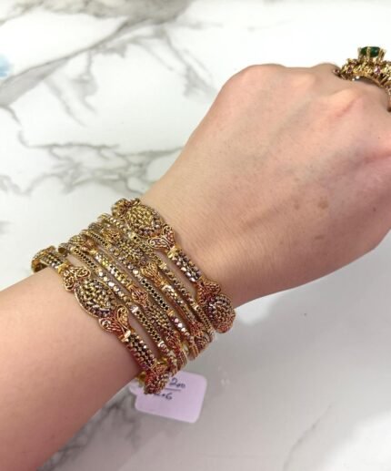 A hand adorned with a beautiful set of antique gold bangles featuring intricate floral and paisley motifs, perfect for traditional and bridal wear.
