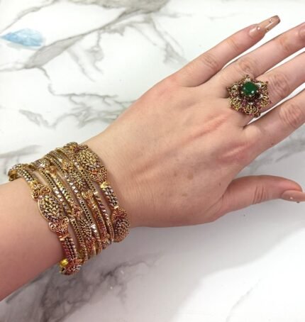 A hand adorned with a beautiful set of antique gold bangles featuring intricate floral and paisley motifs, perfect for traditional and bridal wear.