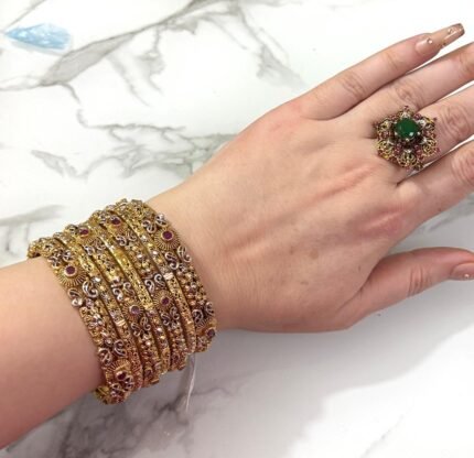 Hand wearing a set of intricately designed gold bangles featuring red stone accents and delicate silver filigree work, perfect for festive or ethnic occasions