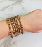 A hand adorned with a set of antique gold bangles featuring intricate dual-tone floral motifs and ruby-colored stone accents, displayed against a marble background.