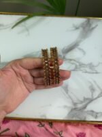 A hand holding a pair of antique gold bangles featuring intricate floral patterns with a dual-tone finish, displayed on a marble background.