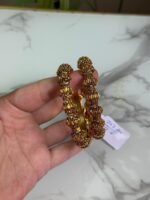 A pair of antique gold plated kada bangles with intricate bulb-shaped temple motifs held in a hand over a marble surface.