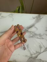 A pair of antique gold bangles with intricate textured design and round pink gemstone centers, held in hand against a marble backdrop.