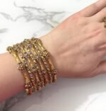 Elegant gold-plated bangle set with intricate floral detailing, beautifully arranged on a woman's wrist for a traditional yet graceful look.