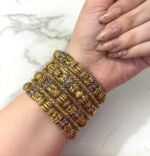 Hand wearing a grand antique gold-plated bangle set with intricate traditional designs and silver detailing, displayed on a marble background.