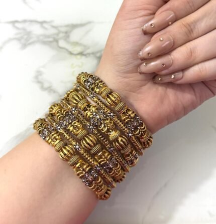 Hand wearing a grand antique gold-plated bangle set with intricate traditional designs and silver detailing, displayed on a marble background.
