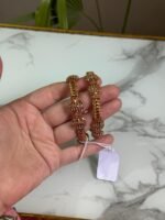 A pair of traditional gold bangles with rope-texture design and ornate bead detailing, held in hand over a marble surface.