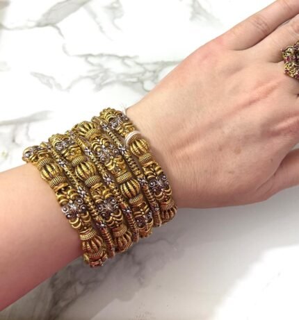 Hand wearing a grand antique gold-plated bangle set with intricate traditional designs and silver detailing, displayed on a marble background.