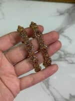 Close-up of intricately designed antique gold bangles held in hand, featuring floral filigree patterns and small pink gemstone embellishments.