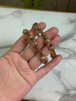 A pair of ornate gold bangles adorned with clusters of multicolor stones in shades of red, pink, and white, held in a hand over a marble background.