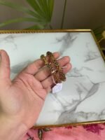 A pair of antique-style gold bangles featuring intricate floral and filigree patterns, held in hand against a marble background.