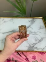 A pair of antique gold bangles featuring large round floral motifs encrusted with pink and white CZ stones, held in a hand over a marble background.