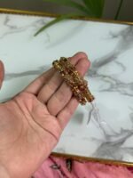 A hand holding two intricately crafted gold bangles featuring antique-style filigree work and floral motifs, with a marble surface in the background.