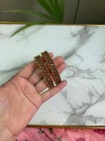 A hand holding a pair of antique gold bangles featuring intricate floral patterns with a dual-tone finish, displayed on a marble background.