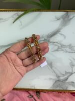 A hand holding two intricately crafted gold bangles featuring antique-style filigree work and floral motifs, with a marble surface in the background.