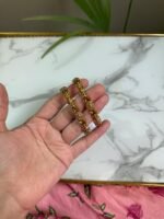 A hand holding two intricately crafted gold bangles featuring antique-style filigree work and floral motifs, with a marble surface in the background.