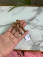 A hand holding two intricately crafted gold bangles featuring antique-style filigree work and floral motifs, with a marble surface in the background.