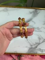 A hand holding two traditional-style gold bangles featuring crown-like ends with red gemstone embellishments and intricate detailing, set against a marble background.