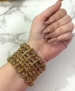 Hand wearing a set of gold-plated crystal bangles with intricate detailing, displayed over a marble tray.