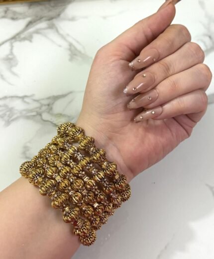 Hand wearing a set of gold-plated crystal bangles with intricate detailing, displayed over a marble tray.