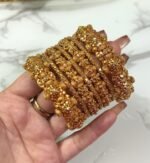 Hand wearing a set of gold-plated crystal bangles with intricate detailing