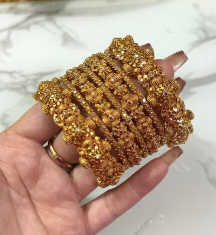 Hand wearing a set of gold-plated crystal bangles with intricate detailing