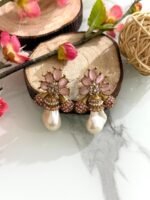 A collection of floral gemstone and pearl drop earrings in multiple colors, including pink, purple, blue, black, and gold, displayed on a white marble surface with decorative flowers and wooden props.