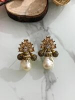 A collection of floral gemstone and pearl drop earrings in multiple colors, including pink, purple, blue, black, and gold, displayed on a white marble surface with decorative flowers and wooden props.