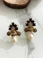 A collection of floral gemstone and pearl drop earrings in multiple colors, including pink, purple, blue, black, and gold, displayed on a white marble surface with decorative flowers and wooden props.