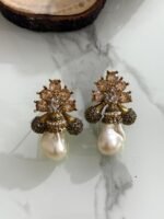 A collection of floral gemstone and pearl drop earrings in multiple colors, including pink, purple, blue, black, and gold, displayed on a white marble surface with decorative flowers and wooden props.