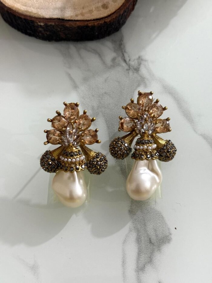 A collection of floral gemstone and pearl drop earrings in multiple colors, including pink, purple, blue, black, and gold, displayed on a white marble surface with decorative flowers and wooden props.