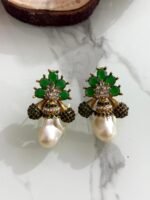 A collection of floral gemstone and pearl drop earrings in multiple colors, including pink, purple, blue, black, and gold, displayed on a white marble surface with decorative flowers and wooden props.