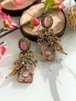 Pair of antique gold earrings with pink oval stones, floral detailing, pearls, and golden leaf motifs, displayed on a marble surface with floral accents.