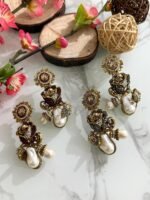 Antique-style drop earrings with rose motif and baroque pearls in maroon and black variants, displayed on a white marble surface with floral and wooden decor.