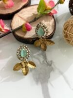 Earrings with mint green teardrop stones, pearl-studded border, and golden leaf design, displayed on a marble surface with floral and wooden decorations.