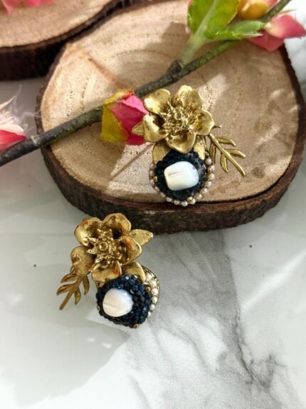 Gold floral stud earrings with navy blue crystal circle and central pearl, accented with a golden leaf.