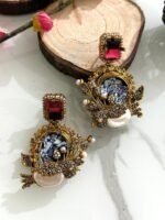 Six ornate earrings with square gemstone studs and circular mosaic centers, decorated with pearl clusters and antique gold detailing, displayed on a marble background.