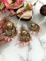 Antique gold maang tikka and earring set with kundan stones and pearl drop embellishments, displayed on a marble surface with floral and wooden decor accents.