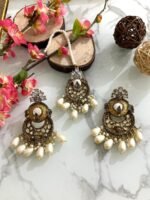 Antique gold maang tikka and earring set with kundan stones and pearl drop embellishments, displayed on a marble surface with floral and wooden decor accents.