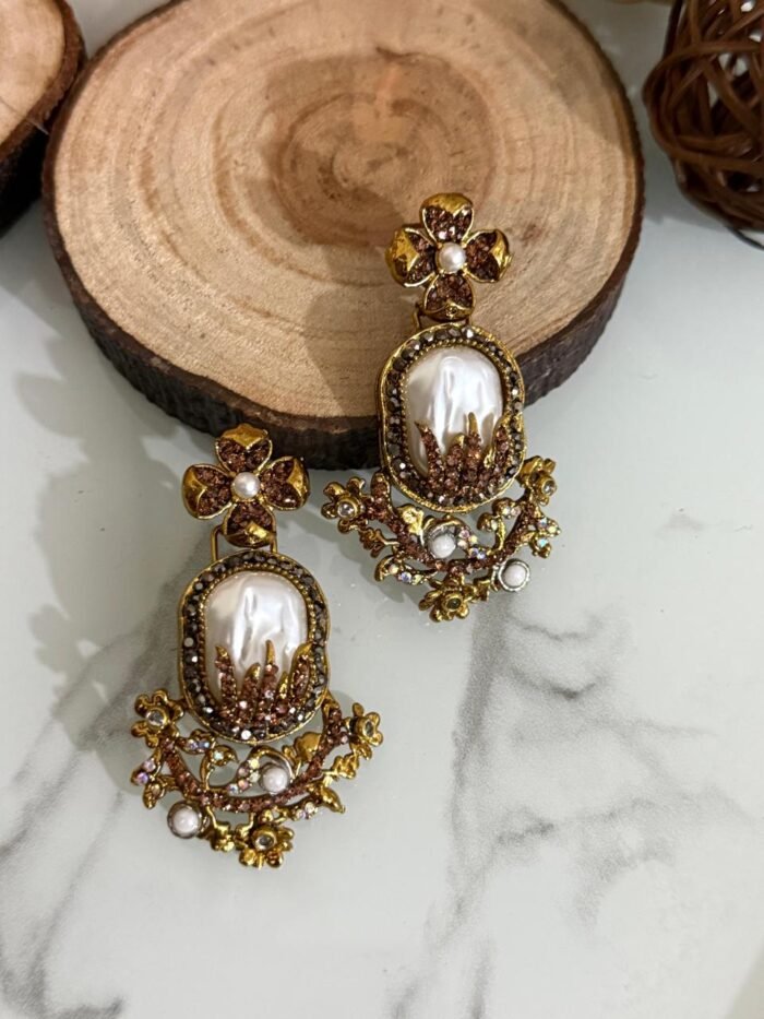 Step into elegance with these Baroque-inspired pearl drop earrings. Featuring a sculpted floral top and ornate golden detailing. Each piece is centered around a lustrous faux pearl with gem-studded accents. Delicate yet bold — perfect for ethnic wear or evening glam. Crafted to capture timeless grace with a garden-fantasy twist.