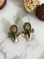 A stylish assortment of embellished pearl drop stud earrings in various jewel tones including red, green, purple, and gold, displayed on a marble surface with rustic wood slices and decorative wicker balls.