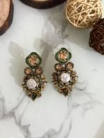 A luxurious collection of ornate antique-finish earrings, each featuring layered floral designs with crystals, faux pearls, and jewel-toned accents, displayed on a marble surface with wood and wicker decor