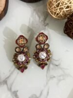 A luxurious collection of ornate antique-finish earrings, each featuring layered floral designs with crystals, faux pearls, and jewel-toned accents, displayed on a marble surface with wood and wicker decor