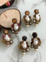 A glamorous set of earrings featuring irregular baroque pearls, large gemstone studs, and floral gold accents with crystal embellishments, displayed on a marble surface with wooden slices for contrast.